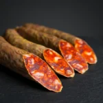 Chorizo Bellota Arturo Sánchez u komadu, s vidljivim crvenim mesom i komadićima masnoće na presjeku.