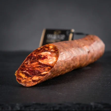 Chorizo Bellota Arturo Sánchez u komadu, s vidljivim crvenim mesom i komadićima masnoće na presjeku.