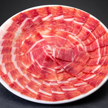 Pršut Bellota 100 % Ibérico Melquiades – Pata negra, tanke šnite složene u krug na bijelom tanjuru