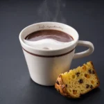 Keramička šalica s vrućom čokoladom koja se dimi i kriškom panetonea Rafa Gorrotxategi na tamnoj podlozi