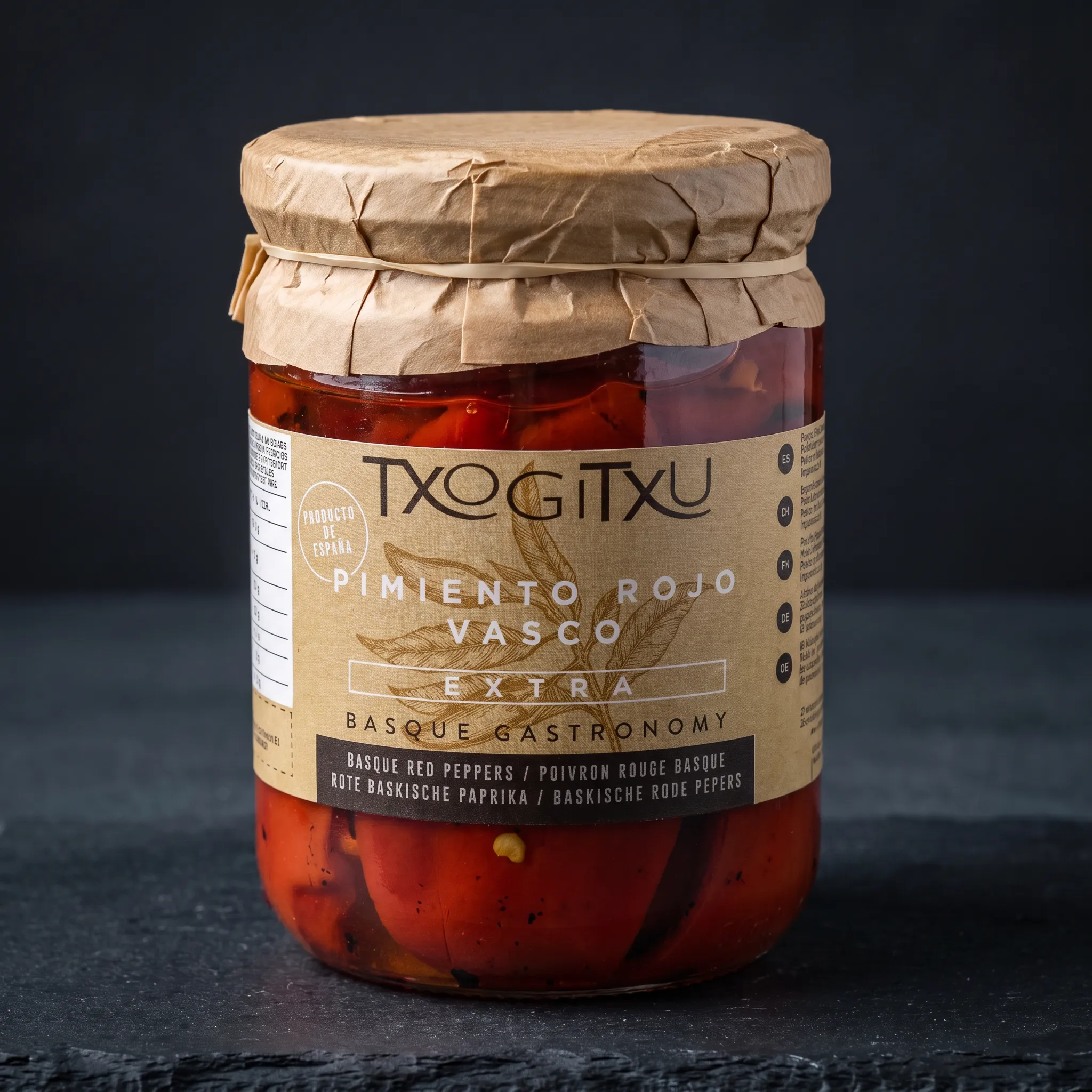 txogitxu-pimiento-di-piquillo Staklenka Txogitxu Pimientos Piquillos Rojos crvenih paprika s papirnatim poklopcem na tamnoj podlozi